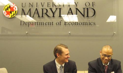 Two men sitting in front of UMD sign